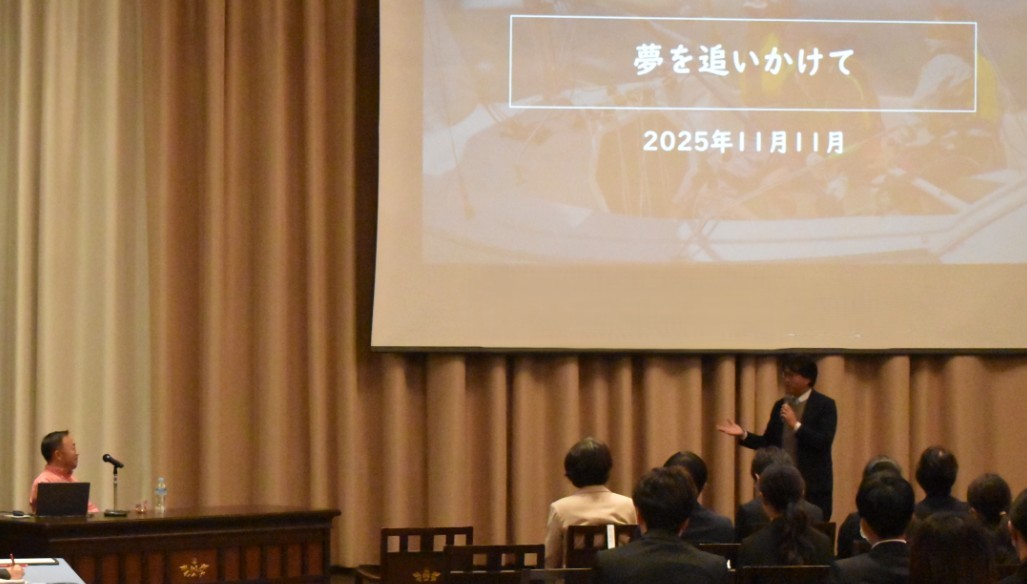 写真:講演会場で登壇者がマイクを手に聴衆へ向けて話しており、前方スクリーンには「夢を追いかけて2025年11月11日」のタイトルが表示されている。